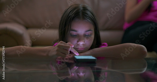 Teenager sitting on couch with smartphone, scene pans to young girl on floor staring at screen, highlighting technology addiction and digital dependence in children