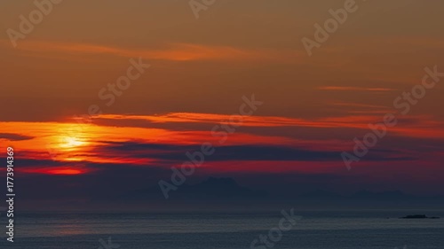 The Midnight Sun rising among the clouds. Hazy summer night by the sea. Time Lapse. Lofoten Islands, Northern Norway.