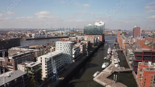 A smooth aerial shot of Hamburg’s HafenCity with its waterfront architecture and the iconic Elbphilharmonie concert hall in the distance, highlighting city redevelopment and cultural growth.