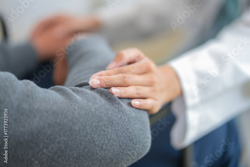 close-up shows a male doctor gently placing his hand on an elderly patient’s back, offering comfort, care, and reassurance during treatment. The compassionate gesture reflects empathy, professionalism