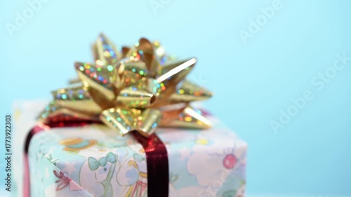 Christmas gift box with golden bow turns and blurs on blue background.