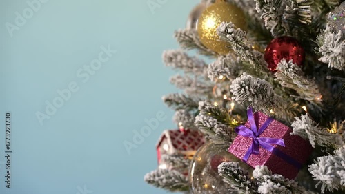 Christmas tree decorations on snowy pine with flashing Christmas lights on blue background.