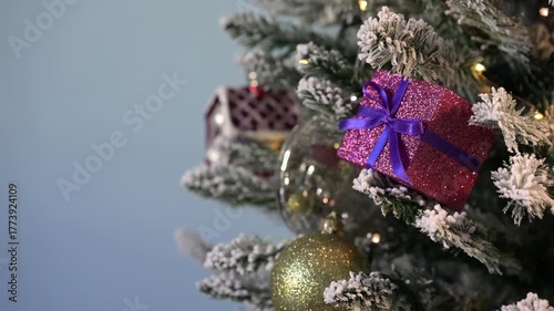 Christmas tree decorations on snowy pine with flashing Christmas lights on blue background.