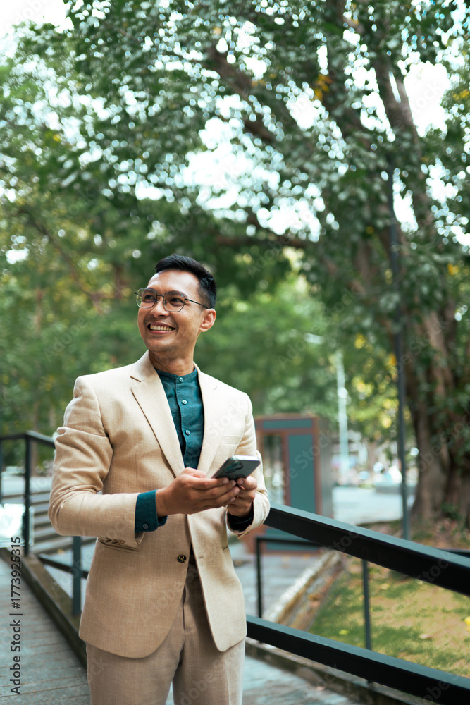 Obraz premium Asian businessman using smartphone, smiling in park