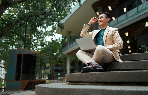 Asian businessman using laptop outdoors feeling successful