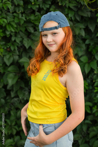 a red-haired curly teenage girl in a yellow T-shirt and a baseball cap on a green background