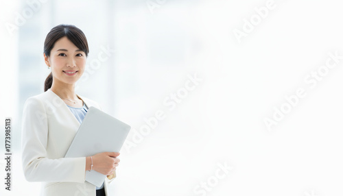 ビジネスシーン：ノートパソコンを抱える若くて美しい女性会社員　白色基調の背景