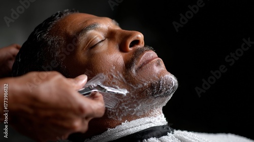 Barber trimming a relaxed man's facial hair with a clipper in a professional grooming session
