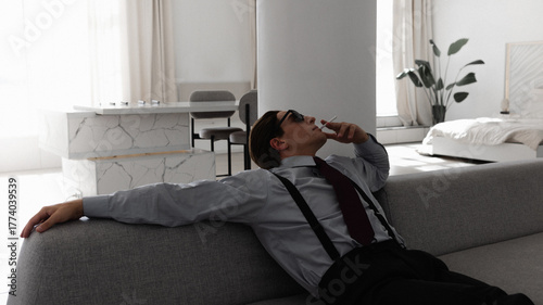 A successful and arrogant young yuppie smokes in his perfect apartment while sitting on the couch