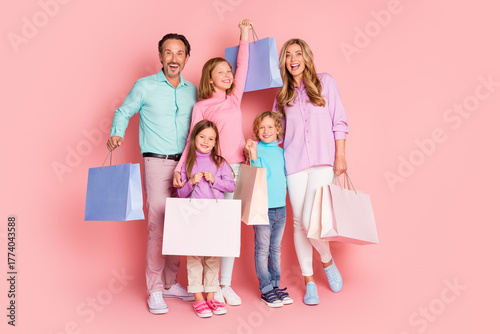 Happy family shopping day with parents and children posing with colorful bags against a pink background
