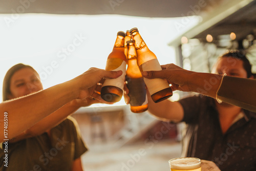 A close-up of a group of Hispanic/Latino friends clinking beer bottles in a joyful toast during golden hour. 