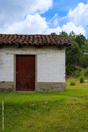 Rustic white house with wooden door in rural area under blue sky with clouds
