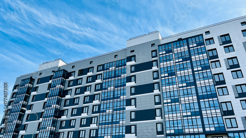 Close-up of the facade of a modern residential building featuring blue and gray panels and large reflective glass windows