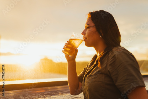 Woman sipping beer at sunset with a warm golden glow