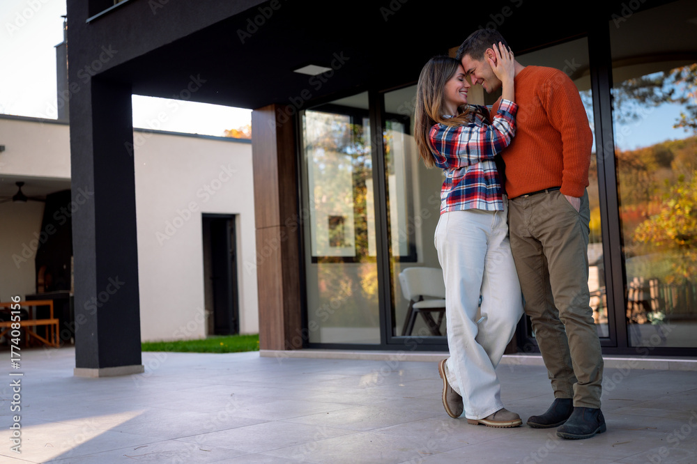 Fototapeta premium Happy young couple embracing each other with affection and love, enjoying a romantic moment together on the patio of their contemporary house, symbolizing romance, relationship, and togetherness