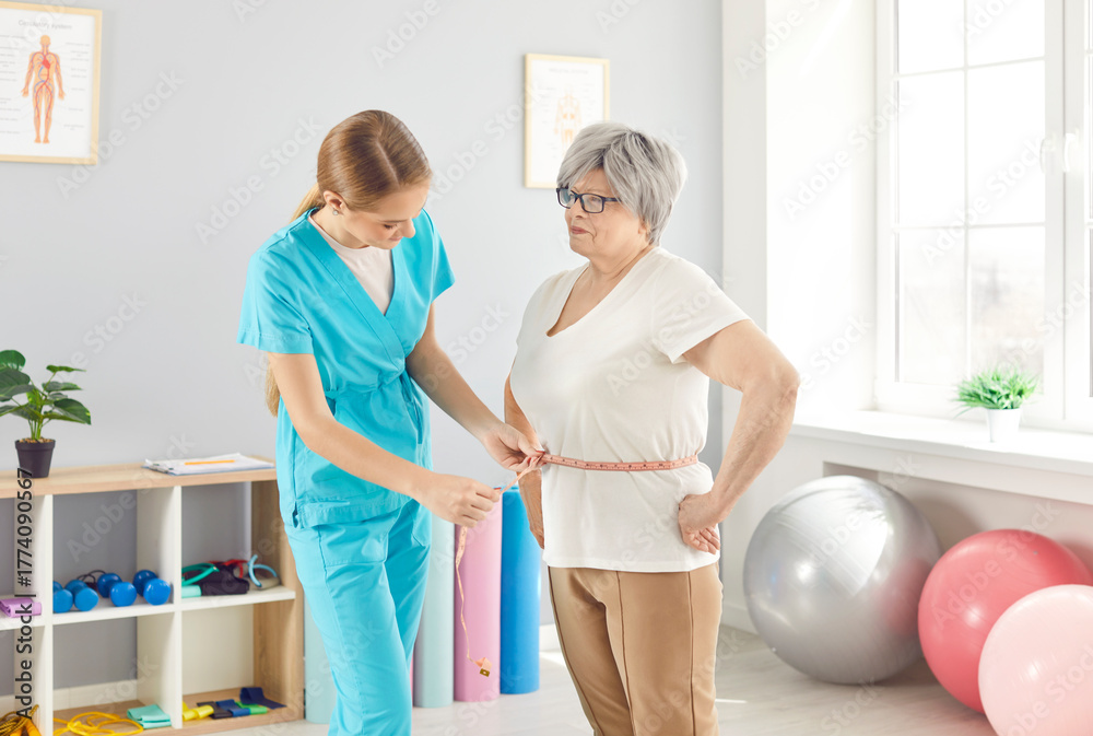 Fototapeta premium Doctor dietitian, or nurse measures the waist of an elderly patient using a tape in a healthcare clinic. Healthcare setting, measuring the waist, and patient care provided by the medical staff.
