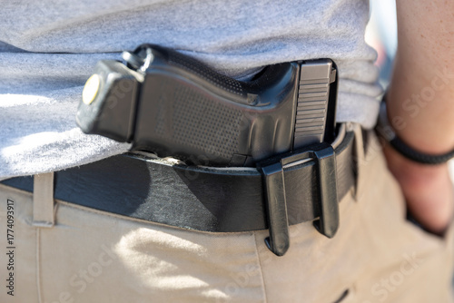 Bild auf Leinwand A  discreet shot of a black handgun tucked into a holster worn on a black belt by a person wearing tan pants and a gray shirt