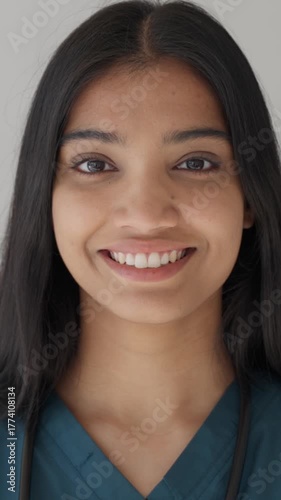 Vertical video. Young indian female doctor in scrubs with stethoscope, smiling confidently in a clean white background headshot