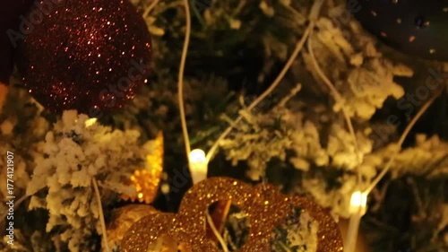 Close-up of Christmas decorations hanging on a Christmas tree with snow and Christmas lights in the background.  