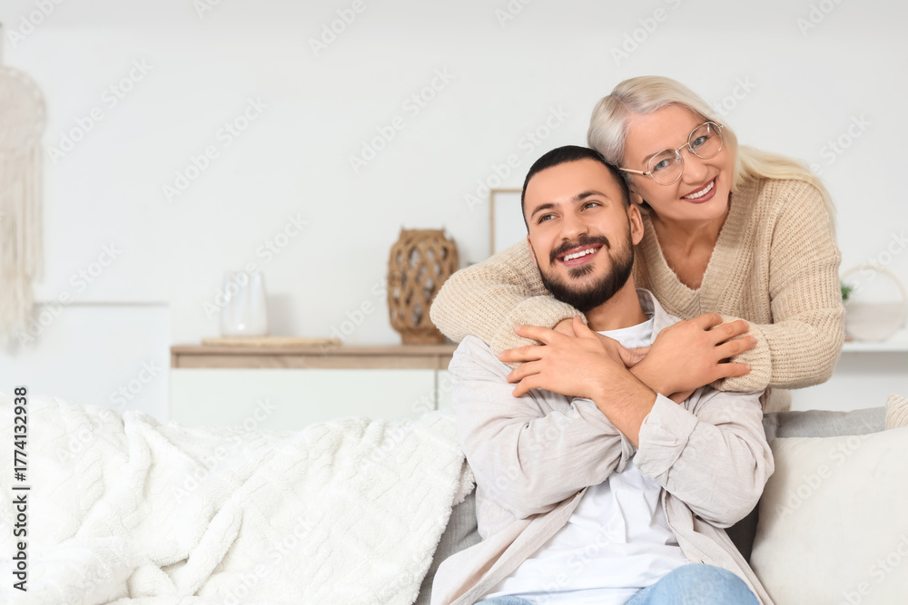 Fototapeta premium Mature woman hugging her son on sofa at home