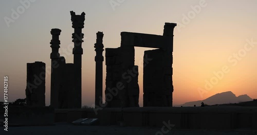 Silhouetted Achaemenid columns and ruined walls at Persepolis as the sun dips behind the Zagros mountains. Quiet desert dusk—heritage, endurance, and the passing of empires.