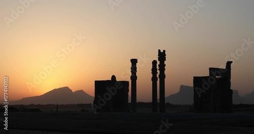Silhouetted Achaemenid columns and ruined walls at Persepolis as the sun dips behind the Zagros mountains. Quiet desert dusk—heritage, endurance, and the passing of empires.