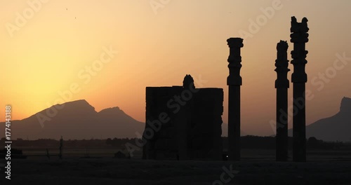 Silhouetted Achaemenid columns and ruined walls at Persepolis as the sun dips behind the Zagros mountains. Quiet desert dusk—heritage, endurance, and the passing of empires.