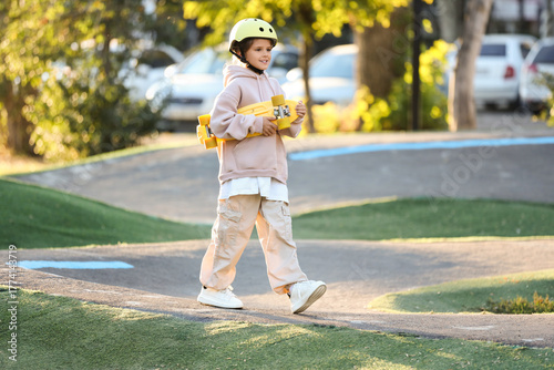 Little girl with helmet and skateboard walking in park