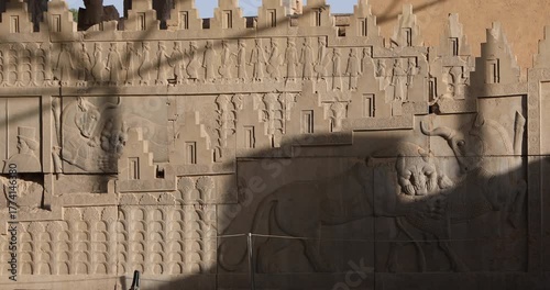 Achaemenid stone relief at Persepolis showing iconic lion attacking bull beside marching Persian guards with spears. Warm late-day light and diagonal shadows emphasize texture and imperial ceremony.