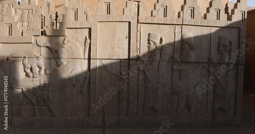Achaemenid stone relief at Persepolis showing iconic lion attacking bull beside marching Persian guards with spears. Warm late-day light and diagonal shadows emphasize texture and imperial ceremony.