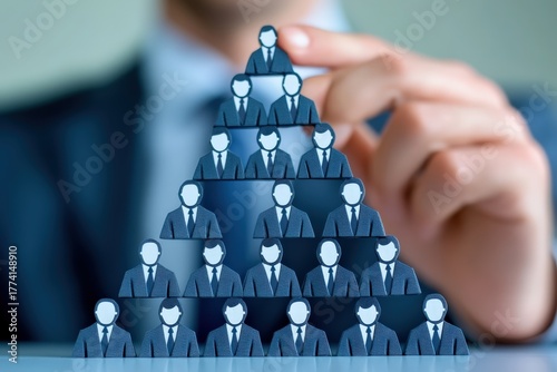 Business Structure Pyramid: A visual representation of business hierarchy, showcasing the organizational structure with the help of miniature figures. A hand placing one figure atop. 