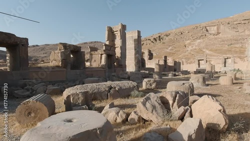 Smooth tracking shot across Persepolis ruins, weaving among toppled column drums and ancient gateways under warm afternoon light—Achaemenid archaeology with a vast desert backdrop.