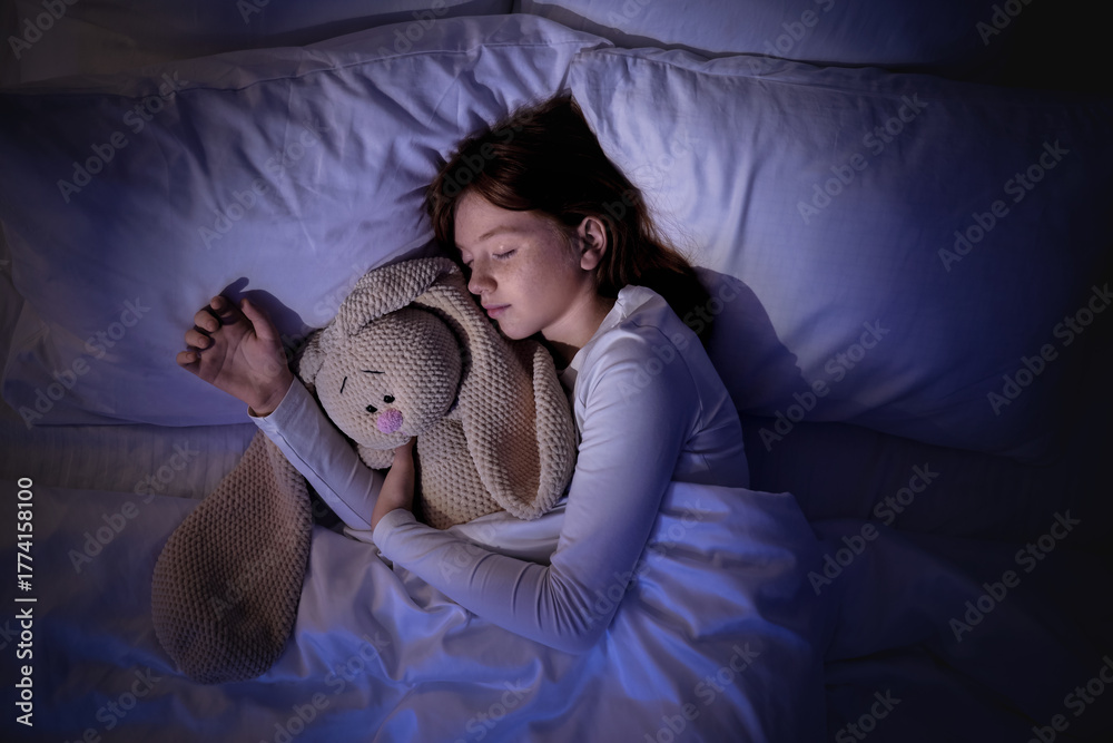 Naklejka premium Cute girl sleeping with bunny toy in bedroom at night