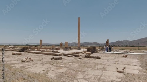 Wallpaper Mural Wide tracking view of Pasargadae palace remains in midday sun: a solitary Achaemenid column rising among stone foundations as a small tour group explores via walkway. Torontodigital.ca