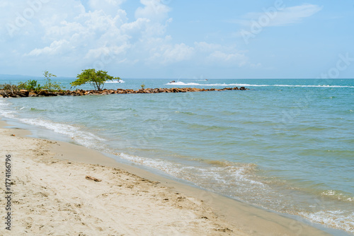 Fototapeta Naklejka Na Ścianę i Meble -  Caribbean beach with calm waves, rocky breakwater and boat in motion, Coveñas coast, Colombia