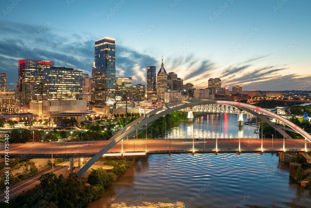 Obraz premium Downtown district of Nashville city in Tennessee, USA at sunset. Cars drive on Korean Veterans Memorial Bridge over Cumberland river. American travel destination.