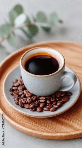Styled Flat Lay Of Roasted Coffee Beans With Espresso In A Textured Gray Cup On A Gray Saucer With Eucalyptus Leaves And A Wooden Tray On A Textured Gray Background