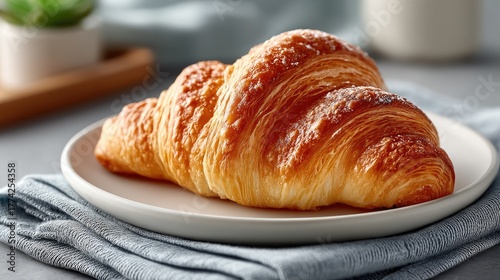 Close-up of a golden brown French croissant sprinkled with colorful sugar crystals resting on a white plate with a textured blue napkin and a blurred green plant in the background studio lighting