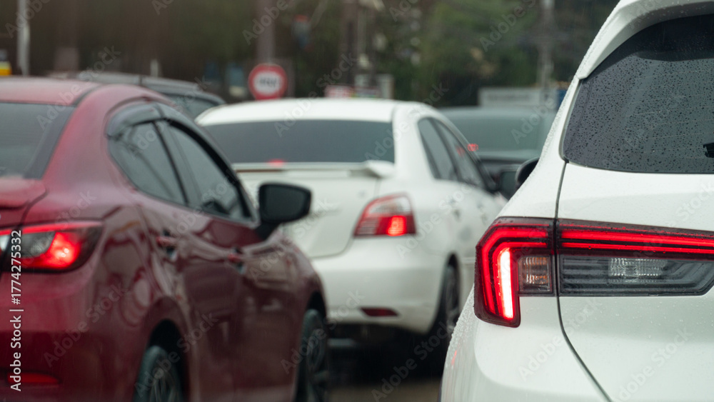 Fototapeta premium Rear side of white car with turn on brake light. Traffic jam on the road after rainy time. on the body of car with drop of water rain. Blurred traffic jam in the city with trees.