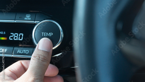 Finger of driving control a Temp button of car. Air conditioner is controlled at 28 degrees Celsius. The front with blurred of car steering wheel.