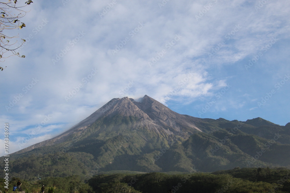 Fototapeta premium Majestic view of a conical volcano rising above lush forested slopes, with its summit transitioning from green vegetation to exposed rock and ash
