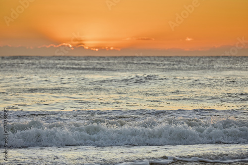 Morning breaks with vivid orange tones lighting the sky, as the waves roll in gently
