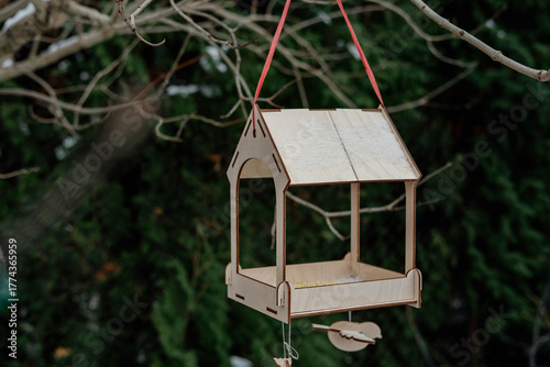 A wooden bird feeder filled with seeds hangs outside in winter