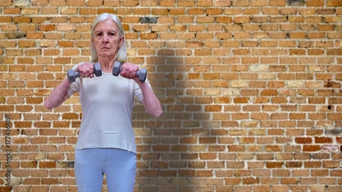Senior Woman Lifting Dumbbells Against Brick Wall