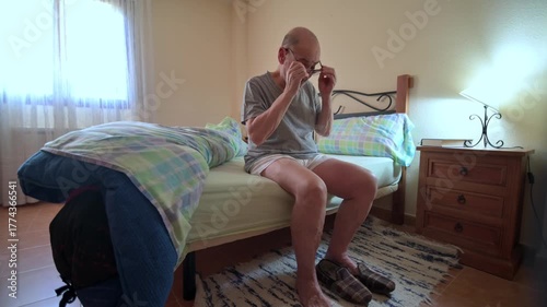 An old man sitting on his bed in his bedroom at dawn after a restful sleep