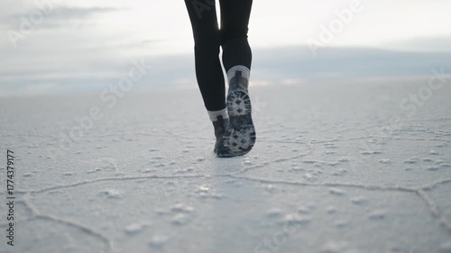 Close up of a woman’s boots walking across the cracked white surface of the Uyuni salt flats in Bolivia during a cloudy morning in slow motion