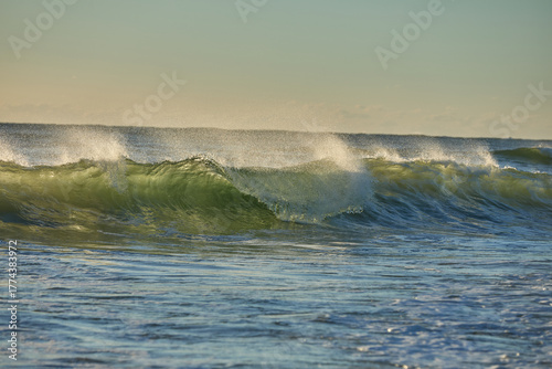 The wind rips the waves, creating a spray, backlit by the early morning sunrise