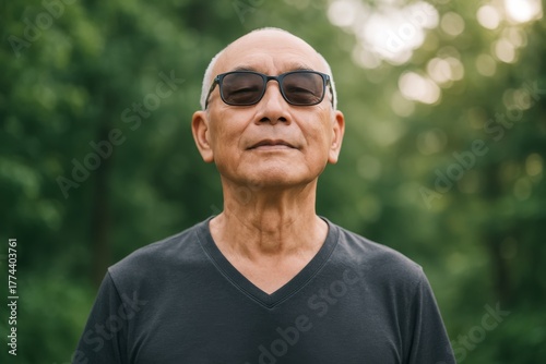 Senior man wearing sunglasses and dark shirt standing peacefully outdoors with eyes closed in forest background, embracing calm lifestyle concept. Ai generative