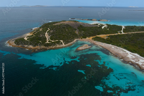 The clear aqua water shows the reef clearly with the mountain tracks leading to the beach
