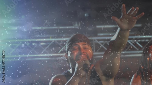 Falling snow revealing lead singer gripping mic and raising arm while concluding concert verse